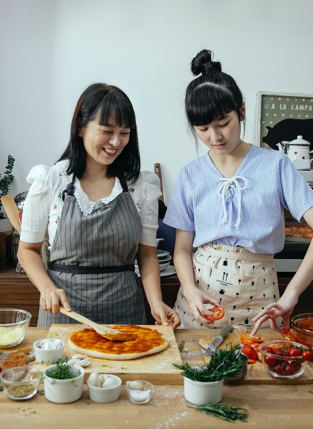Gambar dua perempuan sedang membuat pizza